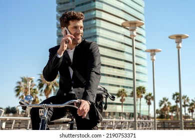 Young Man In A Suit Riding A Classic Bicycle Talking On His Smart Phone In The City