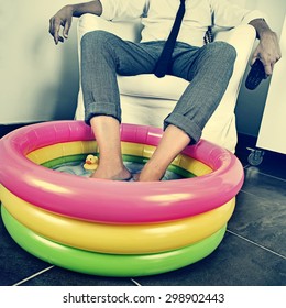 A Young Man In Suit Soaking His Feet In An Inflatable Water Pool Indoors, With A Dramatic Effect, Depicting The Concept Of Staying At Home On Vacation