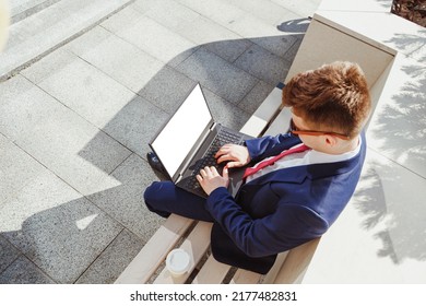 Young Man In Suit Using Laptop With Blank Screen Sitting On Stone Bench. View From Above, Mockup. Man Using Laptop For Online Working, Stock Market Trader