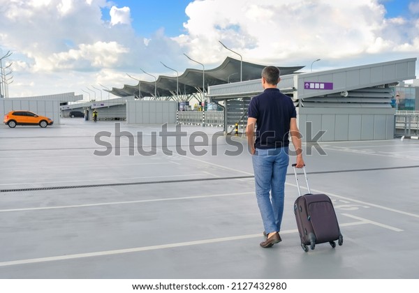 A young man with a suitcase walks in the
parking lot outdoors.