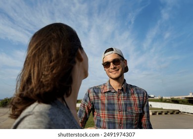 A young man with sunglasses and a cap smiles in love with his girlfriend. Blue sky background with copy space                               - Powered by Shutterstock