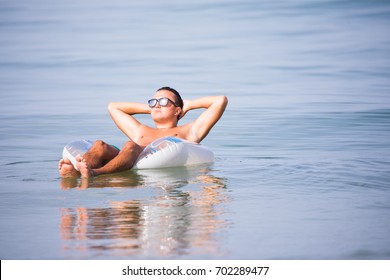 Young Man In Sunglasses With A Glass Of Beer Floating On Rubber Ring In The Ocean Water