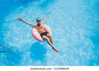 A young man in sunglasses and shorts is relaxing on an inflatable donut in the pool. Summer vacation - Powered by Shutterstock