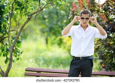 Young Man In Sunglasses In Summer Park. Nature Blurred Background