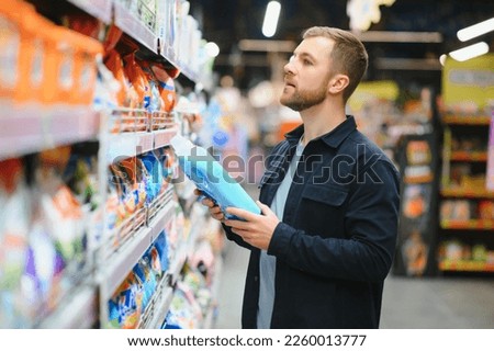 Young man in the supermarket in the household chemicals department. Large selection of products. A brunette in a glasses and a beard in a beige coat