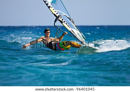 Young man surfing the wind and touching water surface with splashes