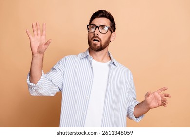 Young man with surprised expression gesturing with hand on beige background