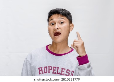 A young man with a surprised expression points his finger upward, representing a sudden idea or realization.