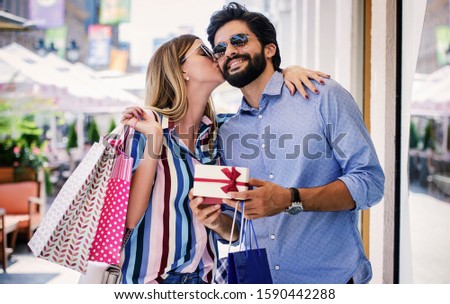 Young man surprised his girlfriend with a present. Attractive young couple enjoying in shopping, having fun in the city. Consumerism, love, dating, lifestyle concept