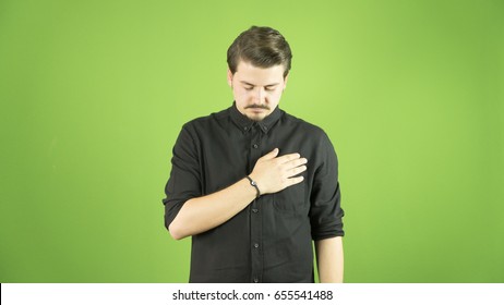 Young man is swearing allegiance with his hand on his chest. Isolated green background.