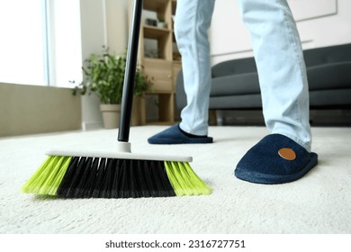 Hombre joven barre la alfombra con escoba en casa, encerrado