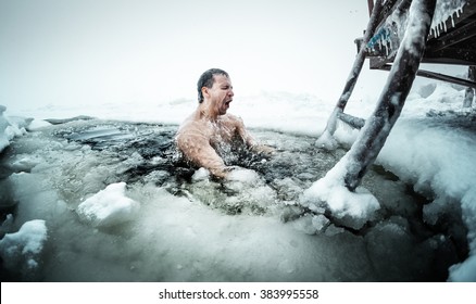 Young man swimming in the ice hole on a winter lake