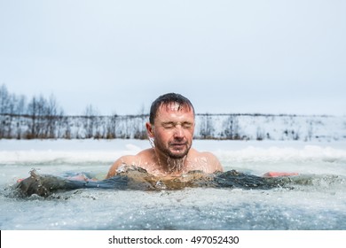 Young man swimming in the winter lake in the ice hole