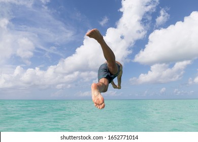 Young Man In Swimsuit Jumping To The Caribbean Sea, Turquoise Water And Blue Sky With White Clouds