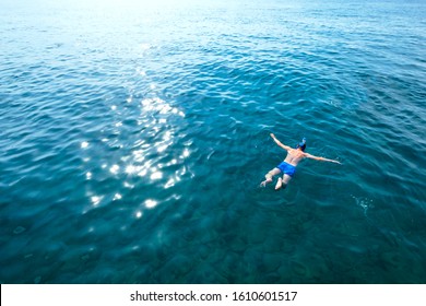 Young man in swimwear lying on blue water. Man in swimming mask relaxing in sea. Tropical summer vacation. Tranquility and peace. Person floating in ocean and watching fish
