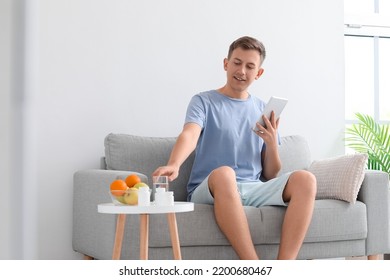 Young Man With Tablet Computer Taking Vitamin Supplement At Home