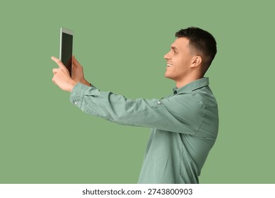 Young man with tablet computer video chatting on green background. Online dating concept
