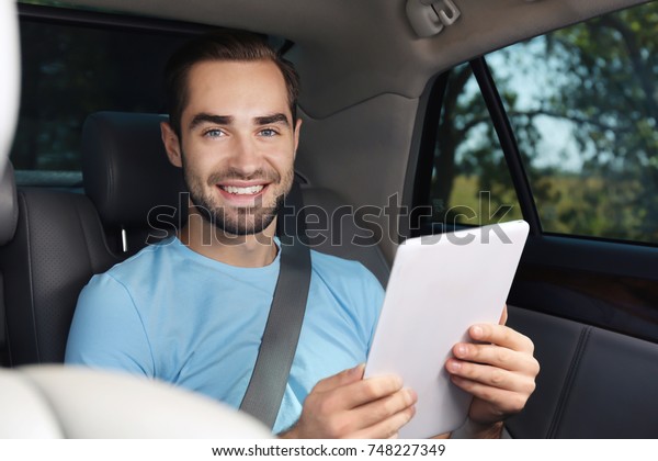Young man with tablet\
on backseat of car