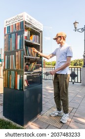 Young man takes books from a free book exchange point on embankment. Rostov-on-Don, Russia, august 07 2021.