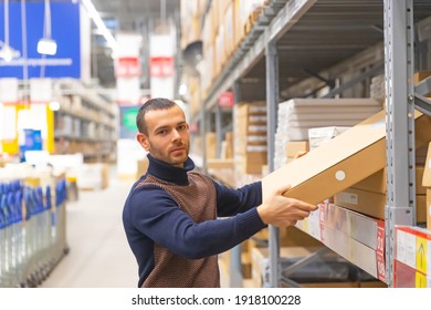 Young Man Takes A Flat Box With Shelf Goods In A Large Store Warehouse