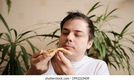 The Young Man Takes A Slice Of Pizza, Takes A Bite With Passion And Chews It. The Guy Looks At A Slice Of Pizza Adoringly. Delicious Cheesy Pizza. 