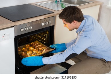 Young Man Taking Baking Tray With Baked Bread From Oven In Kitchen