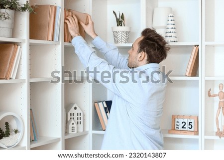 Young man taking book from shelf at home