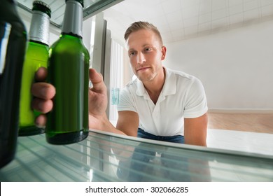 Young Man Taking Bottle Of Beer From A Refrigerator At Home