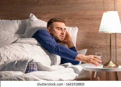 Young Man Taking Glass Of Water From Bedside Table At Night