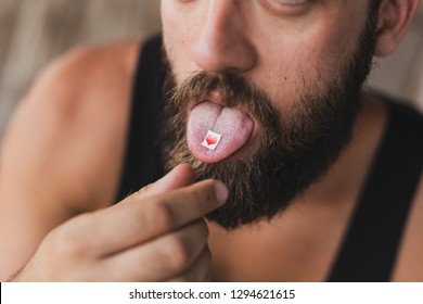 Young man taking LSD; LSD card on a man's tongue. Focus on the LSD stamp