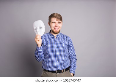 Young Man Taking Off Plain White Mask Revealing Face, Gray Background