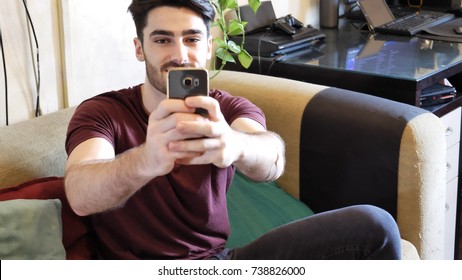 Young Man Taking Photo Of Person Behind Camera, Seen From The Point Of View Of Who Is Being Photographed. At Home, Indoor