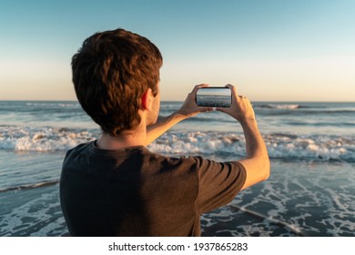 Young man taking a picture of the sea with his smartphone.  - Powered by Shutterstock