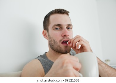 Young Man Taking A Pill In His Bedroom