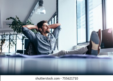 Young man taking rest and listening music while sitting in office. Male designer sitting relaxed at his workplace. - Powered by Shutterstock