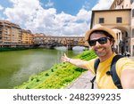 Young man taking selfie in front of Ponte Vecchio bridge in Florence Tuscany Italy, during her summer vacations in Europe.