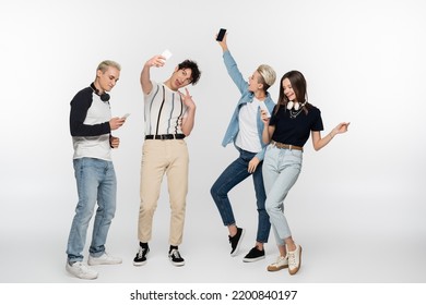 Young Man Taking Selfie And Showing Victory Sign Near Friends With Smartphones Dancing On Grey Background