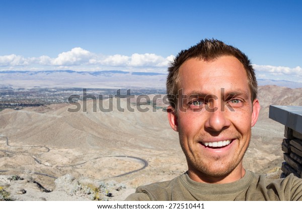 young man taking a selfie with the view of the\
desert valley in southern\
California