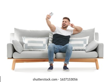 Young man taking selfie while sitting on sofa against white background