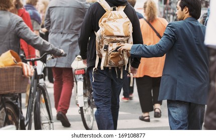 Young man taking wallet from backpack of a man walking on street during daytime. Pickpocketing on the street during daytime