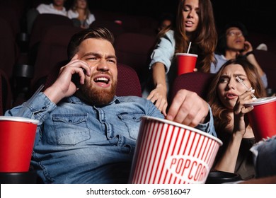 Young Man Talking Loud On Mobile Phone While Watching Movie At The Cinema And Disturbing Audience