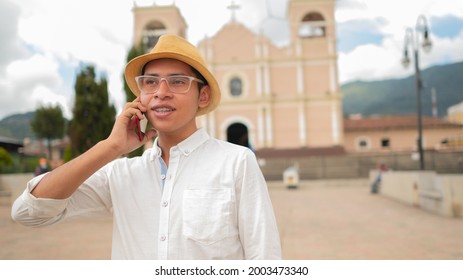 Young Man Talking On A Cell Phone In The Central Park Of Totonicapán Guatemala With The Church Behind.