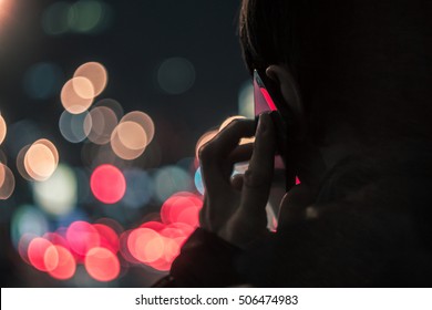 Young Man Talking On Mobile Phone At Night In Front Of Blurred City Lights