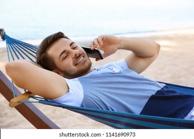 Young Man Talking On Phone In Hammock At Seaside