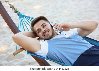 Young Man Talking On Phone In Hammock At Seaside