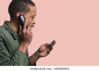 Young Man Talking On The Phone And Reading A Card In His Hand On A Plain Background