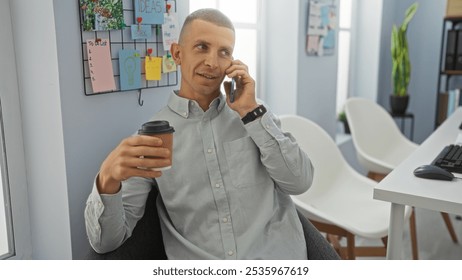 Young man talking on phone while holding a coffee cup in an office with a bulletin board in the background and bright natural light. - Powered by Shutterstock