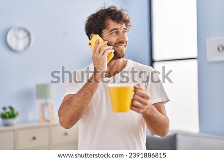 Young man talking on smartphone drinking coffee at home