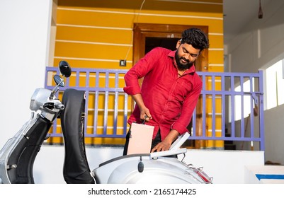 Young man talking out electric scooter battery from bike dicky for recharging near home - concept of problems with battery charging - Shutterstock ID 2165174425