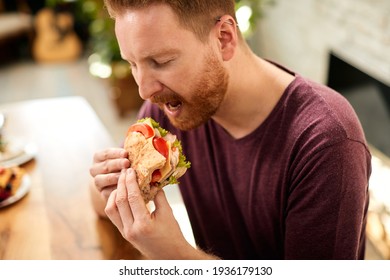 Young Man Tasting Sandwich With Eyes Closed While Eating At Home.